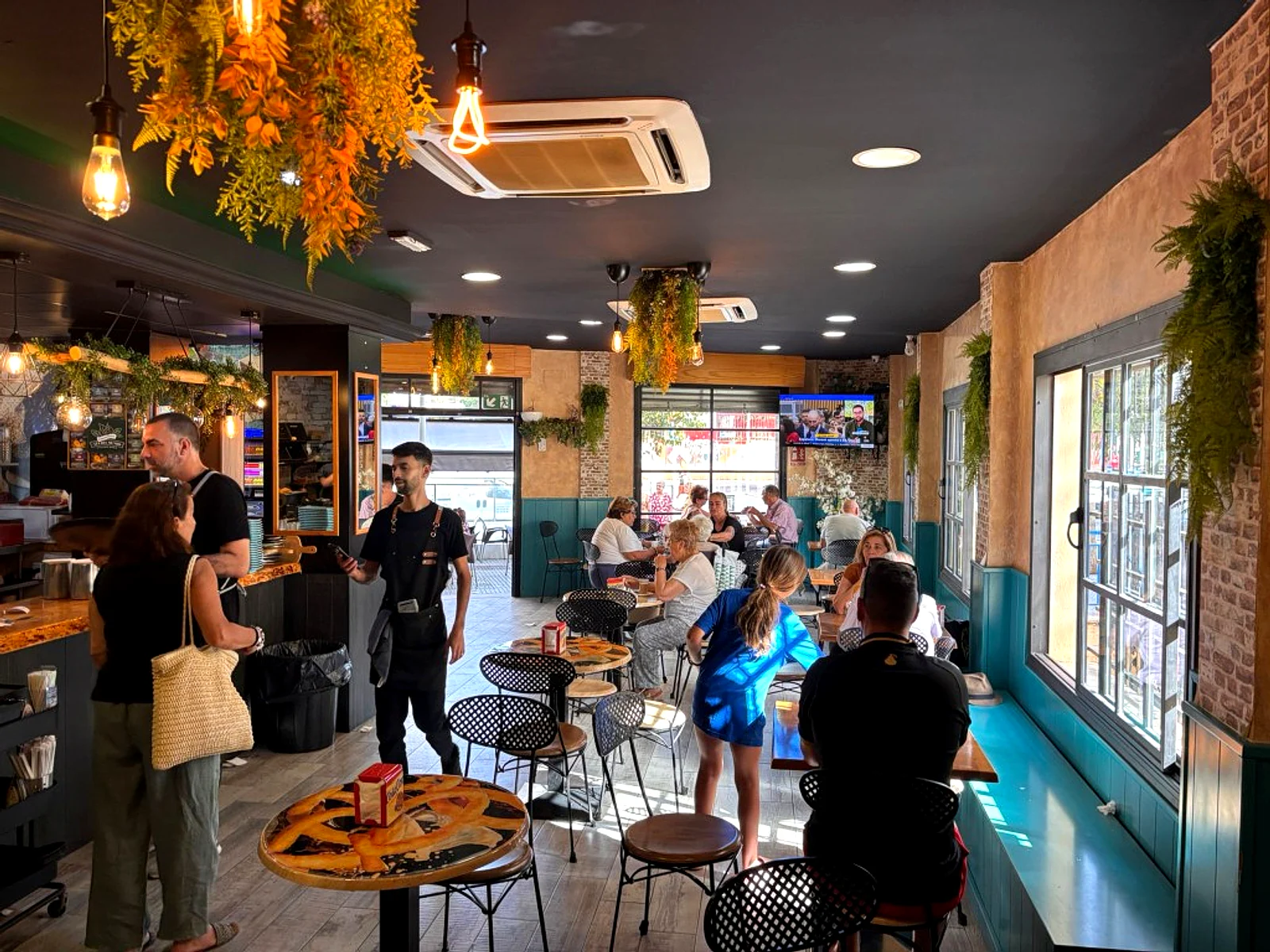 Salón de La Tradición con mesas redondas, plantas colgantes y clientes, Málaga